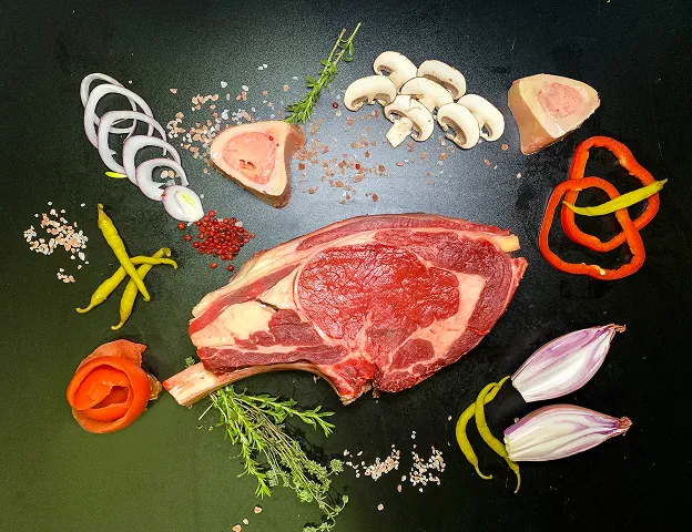 Une côte de bœuf crue entourée de champignons, légumes, herbes et assaisonnements Le Passage près d'Agen dans le Lot-et-Garonne 47